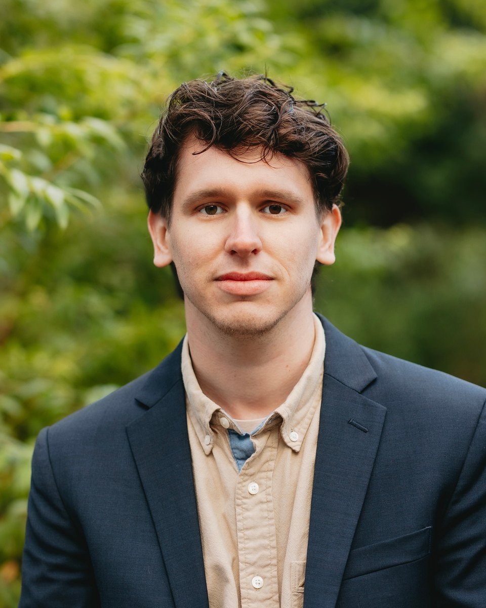 Caleb Grimes, in a navy blazer and tan shirt, outdoors in a garden